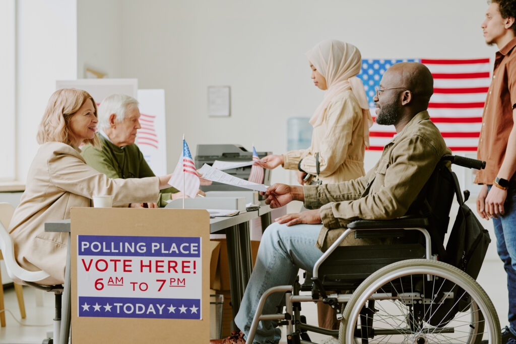 Side view shot of Black man with disability and Muslim woman taking ballot papers at polling station on election day